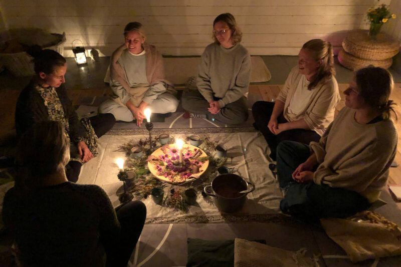 Flera kvinnor sitter på golvet runt ett fat med ett tänt ljus. Pågår en cacaocermoni under Wise Woman Retreat i Järvsö. 